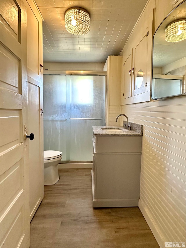 bathroom with hardwood / wood-style flooring, toilet, wooden walls, vanity, and an enclosed shower