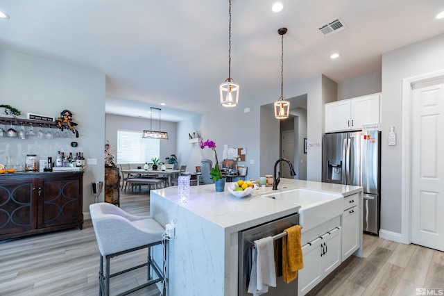 kitchen featuring appliances with stainless steel finishes, an island with sink, white cabinetry, light hardwood / wood-style floors, and pendant lighting