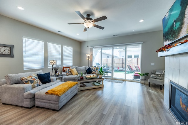 living room featuring light hardwood / wood-style flooring, a tile fireplace, and ceiling fan