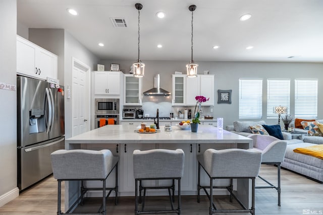 kitchen featuring wall chimney range hood, appliances with stainless steel finishes, white cabinetry, and a breakfast bar area