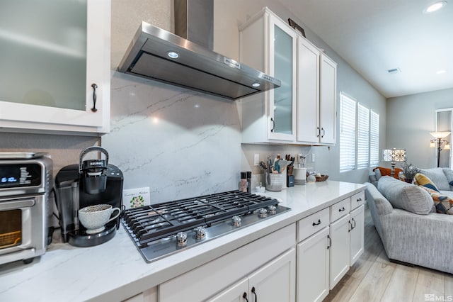 kitchen featuring white cabinets, wall chimney exhaust hood, light hardwood / wood-style flooring, and stainless steel gas stovetop