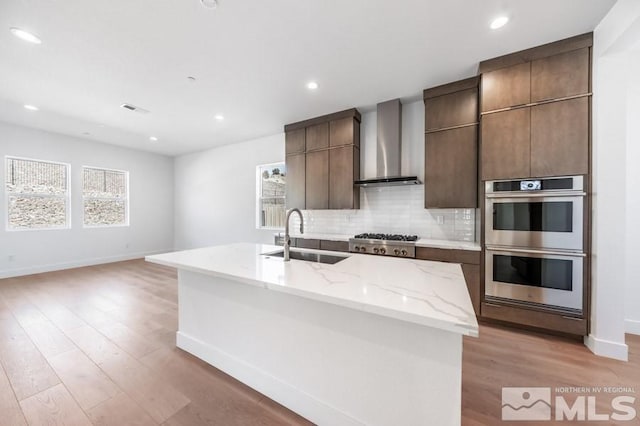 kitchen with a kitchen island with sink, sink, wall chimney exhaust hood, and appliances with stainless steel finishes