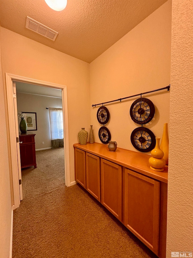 hall featuring a textured ceiling and dark carpet