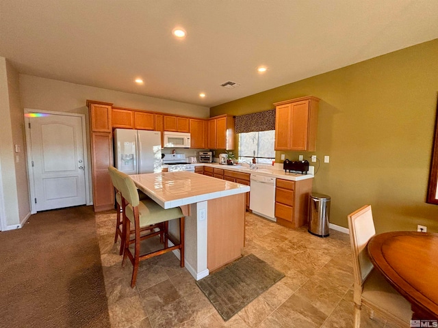 kitchen with light carpet, a kitchen island, a kitchen breakfast bar, tile countertops, and white appliances