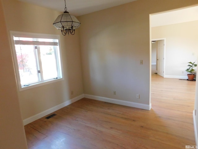 empty room with a chandelier and light wood-type flooring