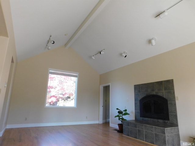 living room with lofted ceiling with beams, a tiled fireplace, wood-type flooring, and rail lighting