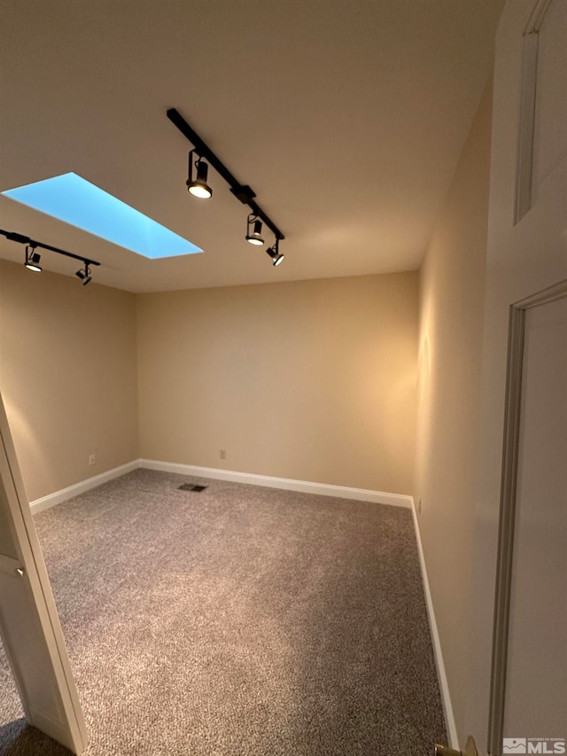 carpeted spare room featuring track lighting and a skylight