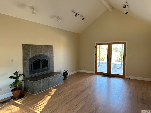 unfurnished living room featuring high vaulted ceiling, french doors, a tile fireplace, rail lighting, and hardwood / wood-style flooring