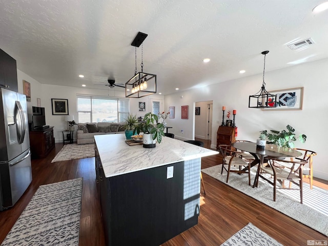 kitchen featuring ceiling fan, a kitchen island, stainless steel refrigerator with ice dispenser, dark wood-type flooring, and a textured ceiling