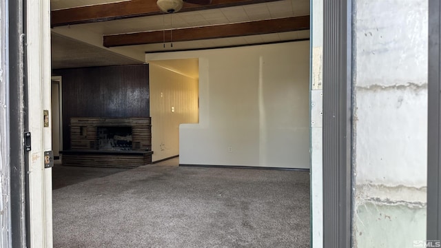 unfurnished living room with carpet floors, a fireplace with raised hearth, and beam ceiling