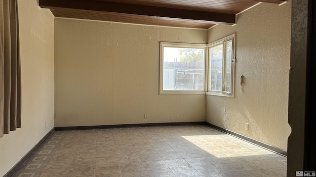 empty room featuring wood ceiling, a textured wall, baseboards, and beam ceiling