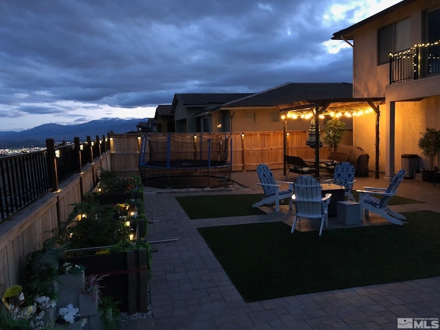 view of yard featuring a mountain view, a patio area, a trampoline, and a fire pit