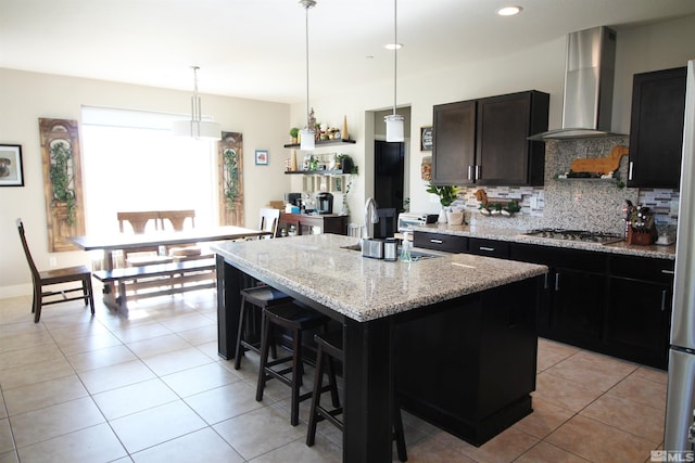 kitchen with wall chimney range hood, a breakfast bar area, a center island, light stone countertops, and stainless steel gas stovetop