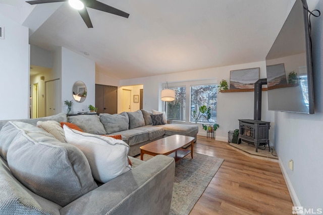 living room featuring a wood stove, lofted ceiling, light wood-type flooring, and ceiling fan