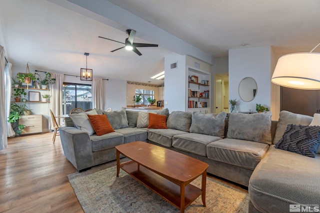 living room featuring ceiling fan with notable chandelier, light wood-type flooring, and built in shelves