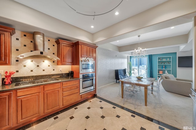 kitchen featuring tasteful backsplash, stainless steel appliances, wall chimney exhaust hood, pendant lighting, and an inviting chandelier