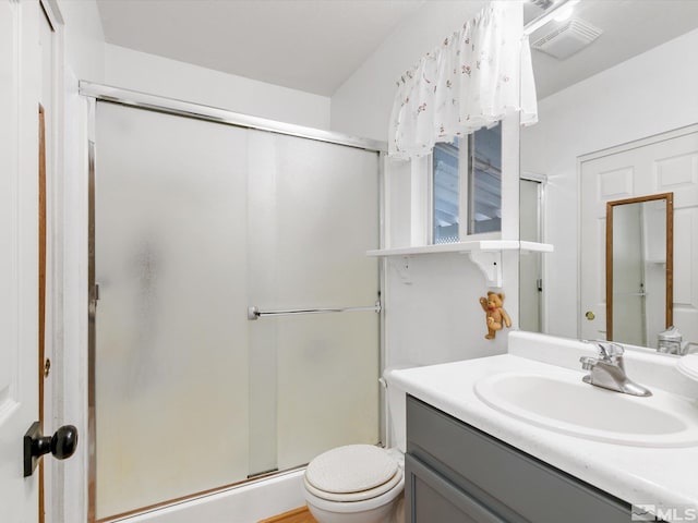 bathroom featuring a shower with door, vanity, and toilet