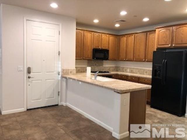 kitchen featuring kitchen peninsula, light stone countertops, and black appliances