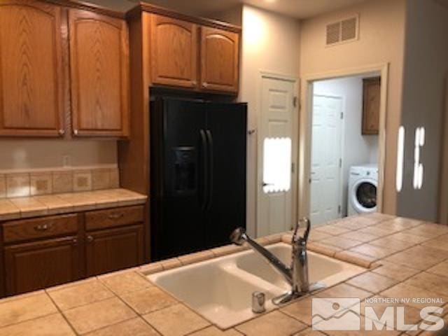 kitchen featuring washer / dryer, sink, tile counters, and black fridge with ice dispenser