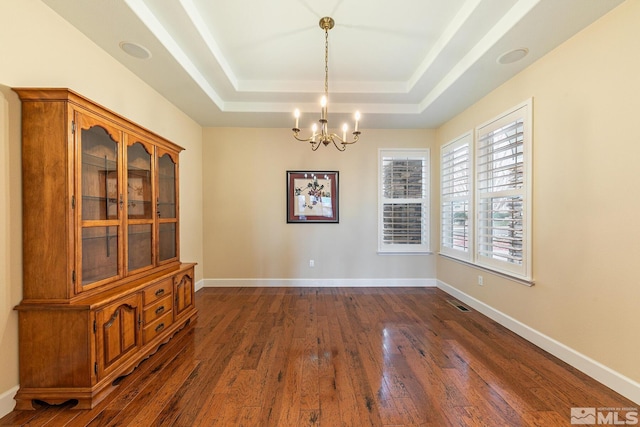 unfurnished dining area featuring dark hardwood / wood-style flooring, a notable chandelier, and a tray ceiling