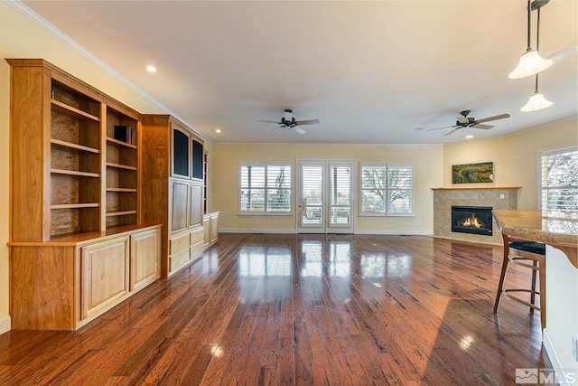 unfurnished living room with dark wood-type flooring, ornamental molding, a healthy amount of sunlight, and a tiled fireplace