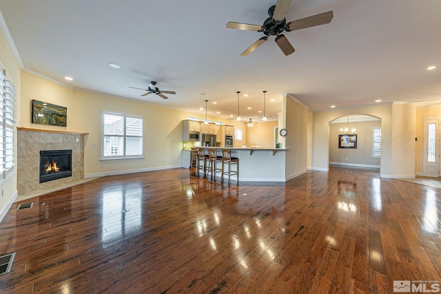 unfurnished living room with crown molding, ceiling fan, dark hardwood / wood-style flooring, and a tiled fireplace