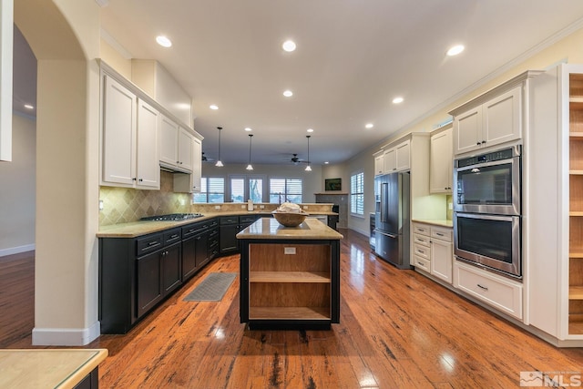 kitchen with hanging light fixtures, a kitchen island, stainless steel appliances, hardwood / wood-style floors, and backsplash