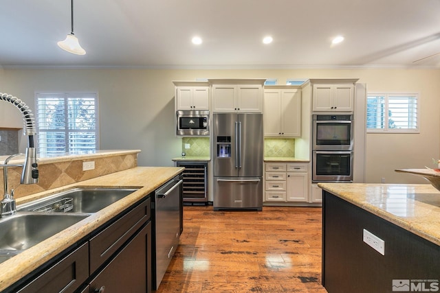 kitchen featuring appliances with stainless steel finishes, sink, wine cooler, hanging light fixtures, and light stone countertops