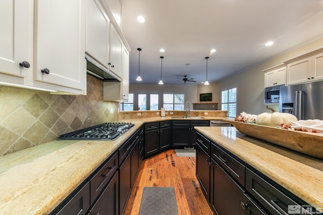 kitchen with sink, light stone counters, decorative light fixtures, stainless steel appliances, and white cabinets