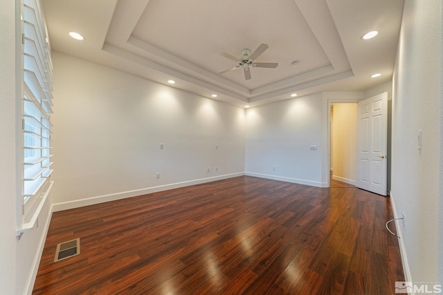 empty room featuring a raised ceiling, dark wood-type flooring, and ceiling fan