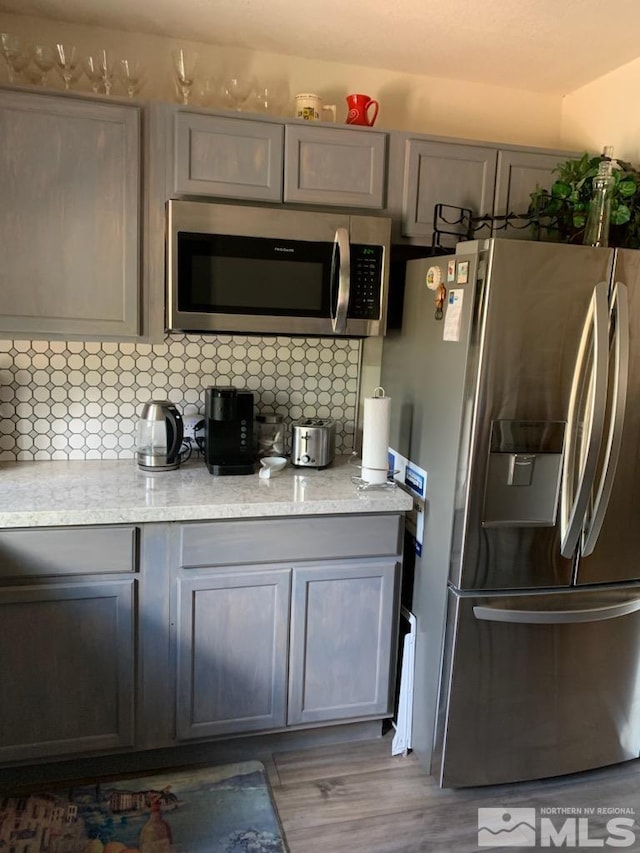 kitchen with gray cabinetry, stainless steel appliances, tasteful backsplash, and light hardwood / wood-style flooring