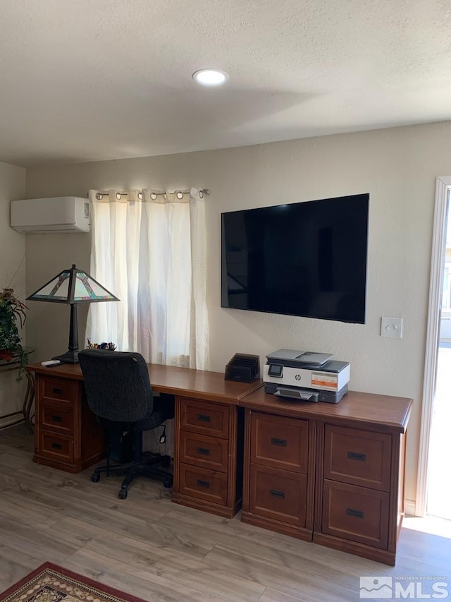 office area featuring a wall mounted AC, a textured ceiling, and light wood-type flooring