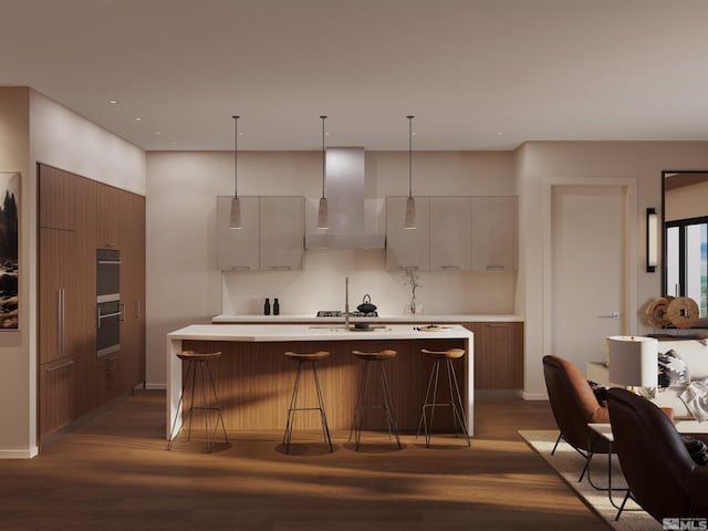 kitchen with decorative light fixtures, dark hardwood / wood-style floors, wall chimney exhaust hood, and a center island with sink