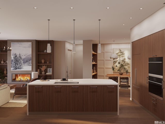 kitchen featuring sink, built in features, double oven, a center island with sink, and dark hardwood / wood-style flooring