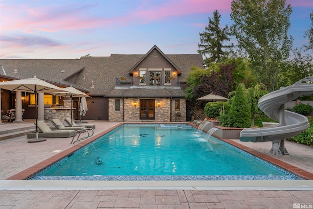 pool at dusk with a water slide, pool water feature, and a patio