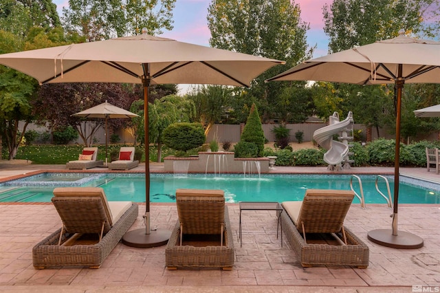 pool at dusk featuring a patio area and pool water feature