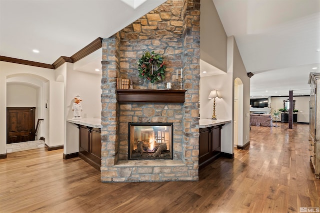 living room with a stone fireplace, ornamental molding, light hardwood / wood-style flooring, and lofted ceiling