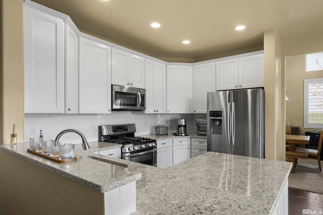 kitchen with appliances with stainless steel finishes, kitchen peninsula, and white cabinets