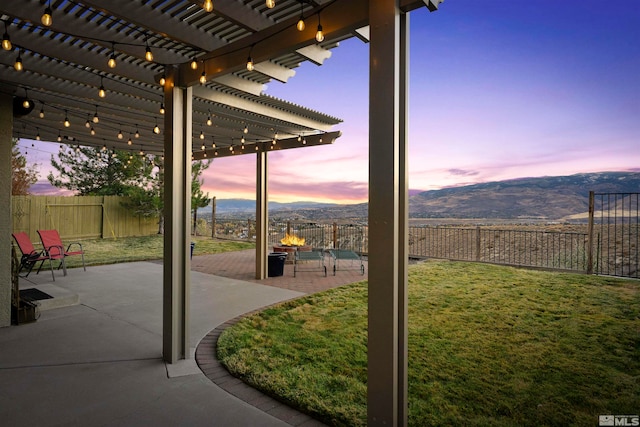 patio terrace at dusk featuring a pergola, a mountain view, and a yard