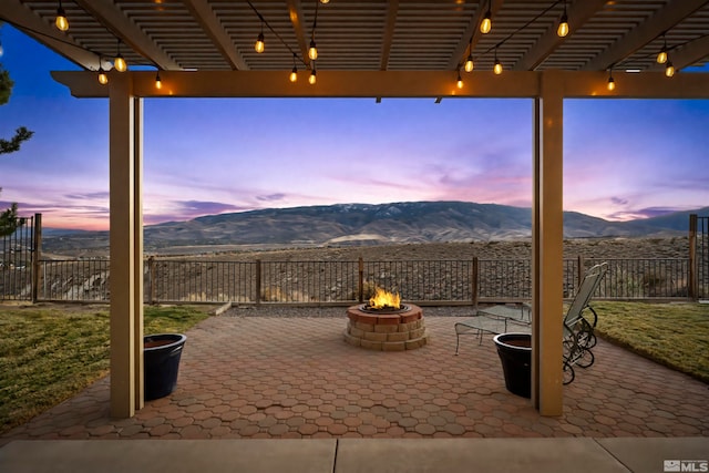 patio terrace at dusk with an outdoor fire pit, a mountain view, and a pergola