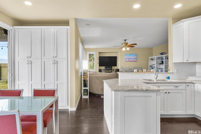 kitchen with light stone countertops, backsplash, ceiling fan, white cabinets, and dark wood-type flooring