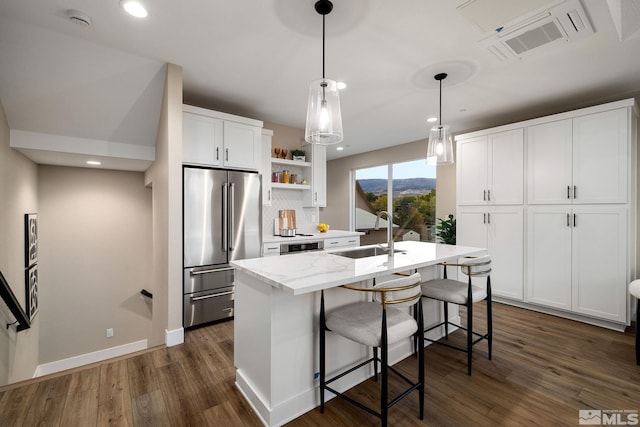 kitchen featuring high quality fridge, sink, an island with sink, and white cabinets