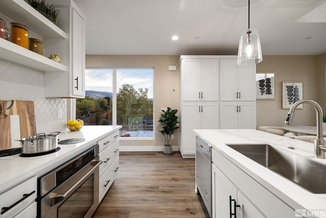 kitchen with stainless steel appliances, sink, light wood-type flooring, white cabinetry, and light stone counters