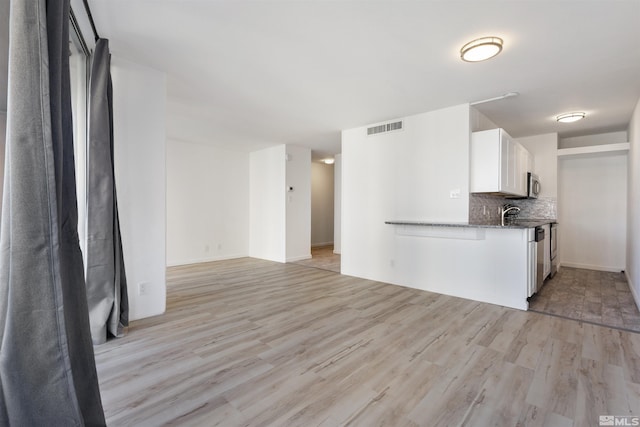 kitchen with decorative backsplash, light hardwood / wood-style floors, white cabinetry, and dark stone counters