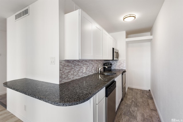 kitchen with kitchen peninsula, white cabinets, stainless steel appliances, and tasteful backsplash