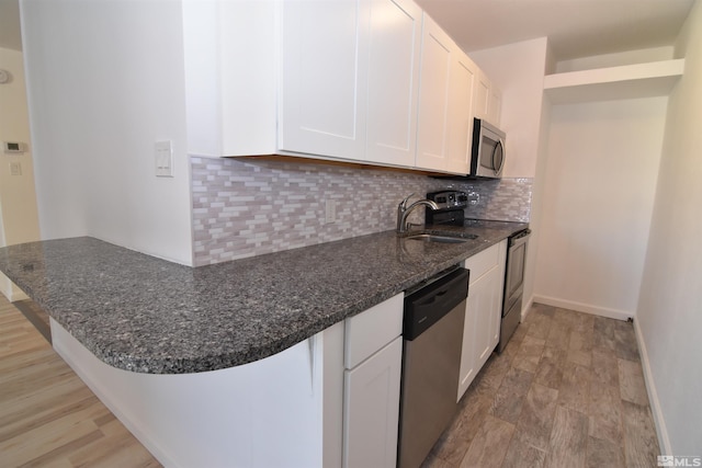 kitchen featuring kitchen peninsula, decorative backsplash, sink, white cabinetry, and stainless steel appliances