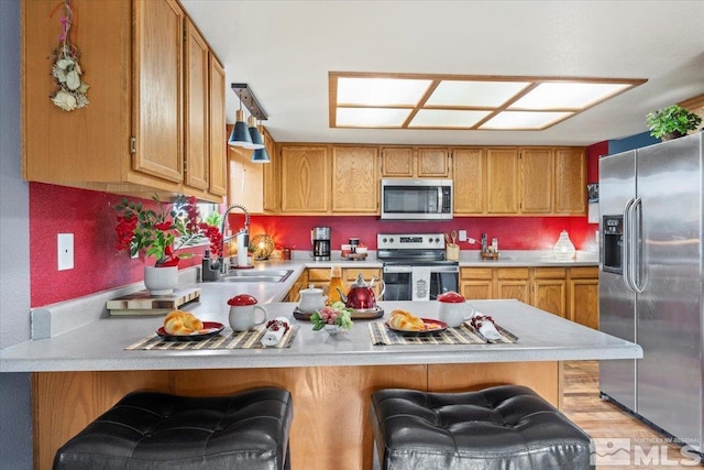 kitchen with appliances with stainless steel finishes, sink, light wood-type flooring, kitchen peninsula, and a breakfast bar