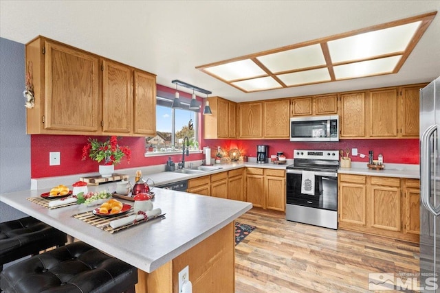 kitchen with kitchen peninsula, stainless steel appliances, sink, decorative light fixtures, and light hardwood / wood-style floors