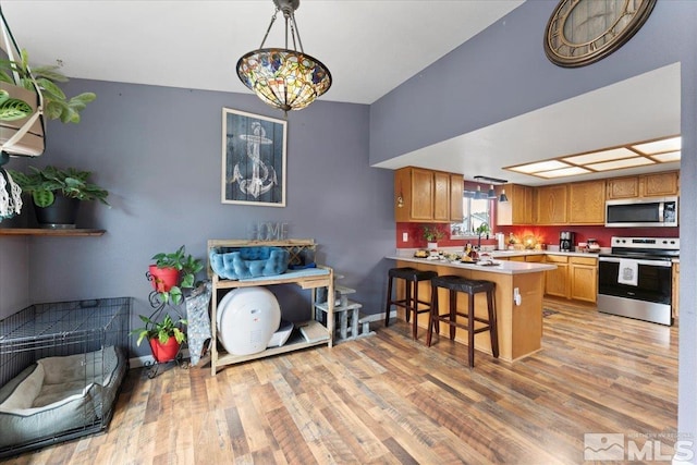 kitchen featuring kitchen peninsula, a breakfast bar, decorative light fixtures, light wood-type flooring, and appliances with stainless steel finishes