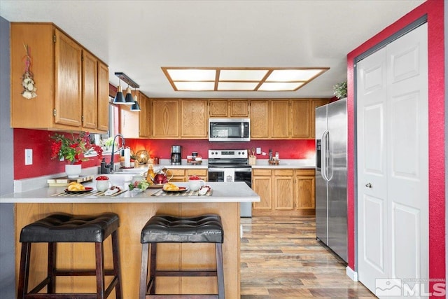 kitchen featuring light wood-type flooring, appliances with stainless steel finishes, kitchen peninsula, and a kitchen breakfast bar